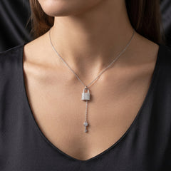 A silver Y-necklace featuring a padlock and key pendant, shown worn on a model's neck over a black satin V-neck top.