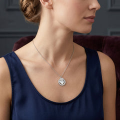 A woman wearing a silver pendant necklace with a circular pendant featuring a stylized bird design, paired with a navy blue sleeveless top.