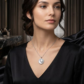 A woman wearing a silver circular pendant necklace with a sunburst design, styled with a black satin V-neck top in an elegant indoor setting.