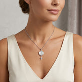 A close-up of a woman wearing a delicate silver necklace with a round white pearl and a small dangling star charm, paired with a cream-colored V-neck top.