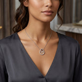 A close-up of a woman wearing a silver teardrop pendant necklace with a clear central stone and a halo of small clear stones, paired with a dark gray V-neck top.