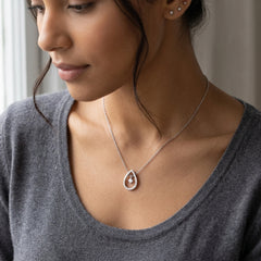 A close-up lifestyle shot of a woman wearing a delicate silver teardrop pendant necklace with a central gemstone, paired with a gray knit top.