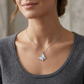 A close-up of a woman wearing a delicate silver chain necklace with a small butterfly pendant. The pendant features a white inlay on one wing and a tiny clear stone on the other.