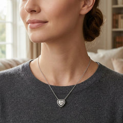 A close-up lifestyle shot of a woman wearing a silver heart-shaped pendant necklace with a double heart design, paired with a dark gray knit sweater.