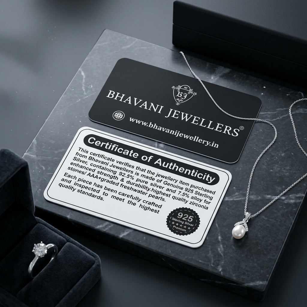 A silver pearl necklace with a delicate chain and bezel-set pearl pendant is displayed on a dark marble surface next to its black presentation box, a black Bhavani Jewellers brand card, and a Certificate of Authenticity. A velvet ring box with a silver ring is partially visible in the lower-left corner.