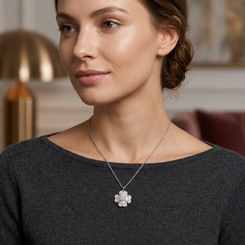 A woman wearing a delicate silver-tone floral pendant necklace with clear stones, styled with a dark gray knit top in a softly lit indoor setting.