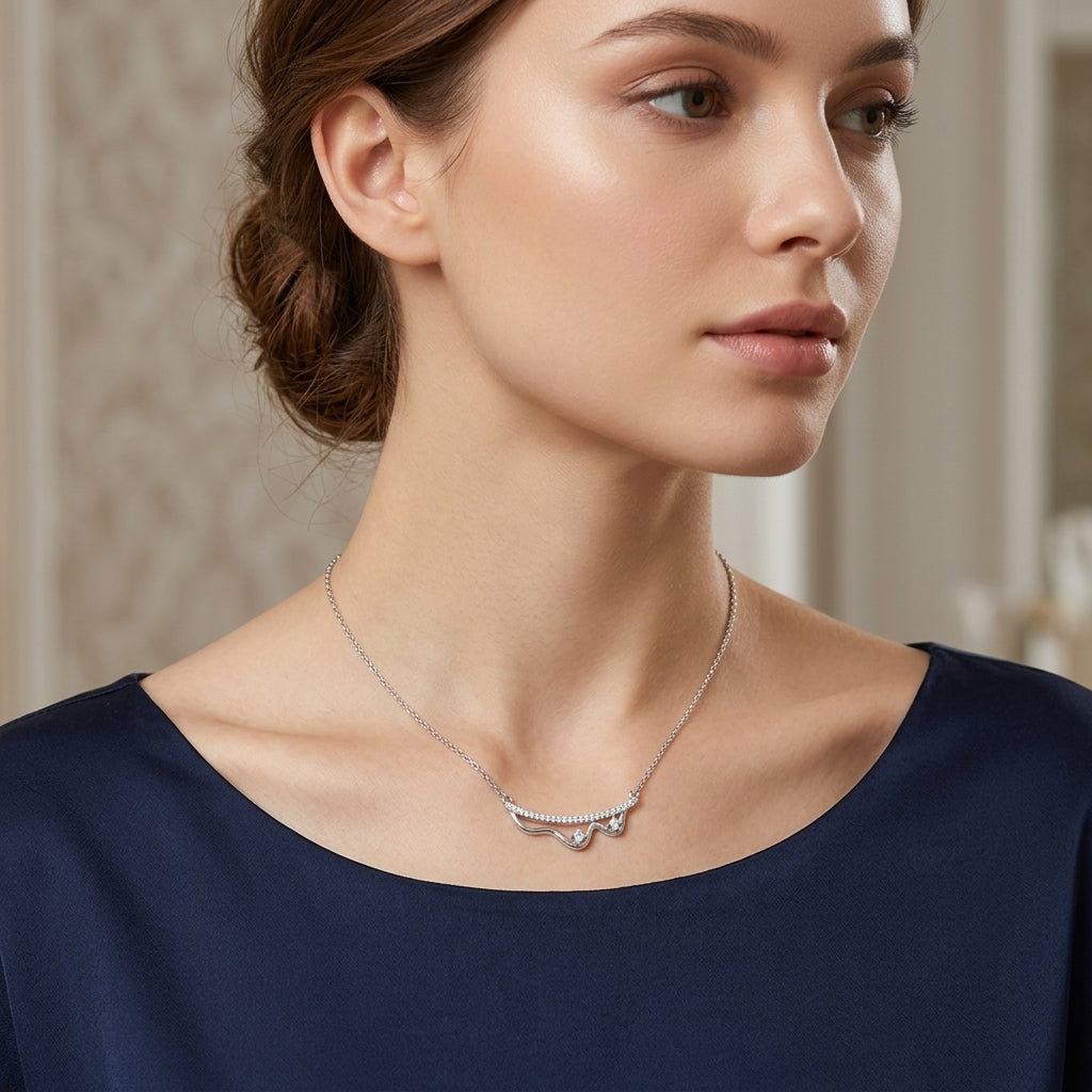 A woman wearing a delicate silver necklace with a small bow-shaped pendant set with clear stones, paired with a navy blue top.