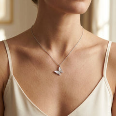 A close-up of a model wearing a delicate silver butterfly pendant necklace on a fine chain, styled with a cream camisole top.