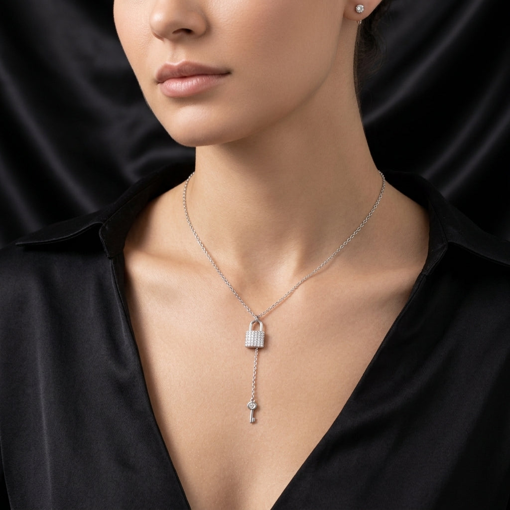 A close-up of a model wearing a silver key-shaped pendant necklace with a padlock at the top, set against a black satin background.