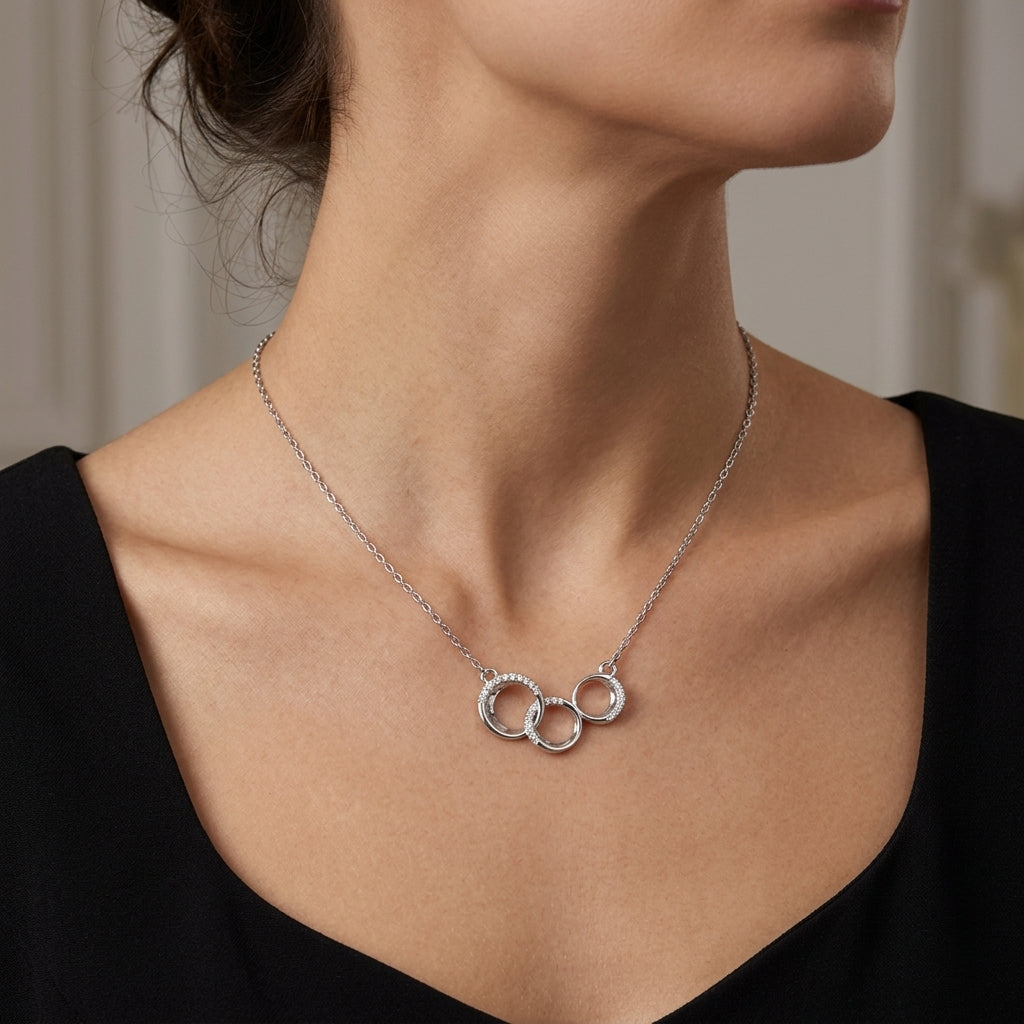 A close-up of a woman wearing a delicate silver chain necklace with three interlocking open rings pendant, styled with a black top.