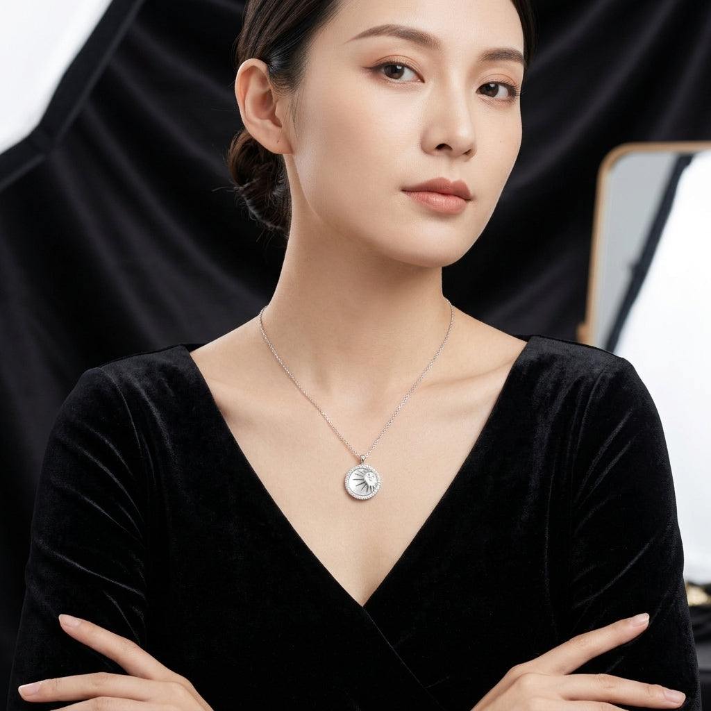 A woman wearing a delicate silver pendant necklace with a circular medallion, styled with a black velvet top against a dark studio backdrop.