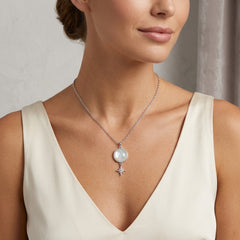 A close-up of a woman wearing a delicate silver necklace with a round white pearl and a small dangling star charm, paired with a cream-colored V-neck top.