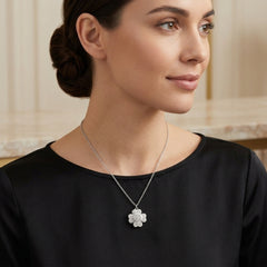 A woman wearing a delicate silver chain necklace with a silver flower-shaped pendant, styled with a black top against a soft beige background.