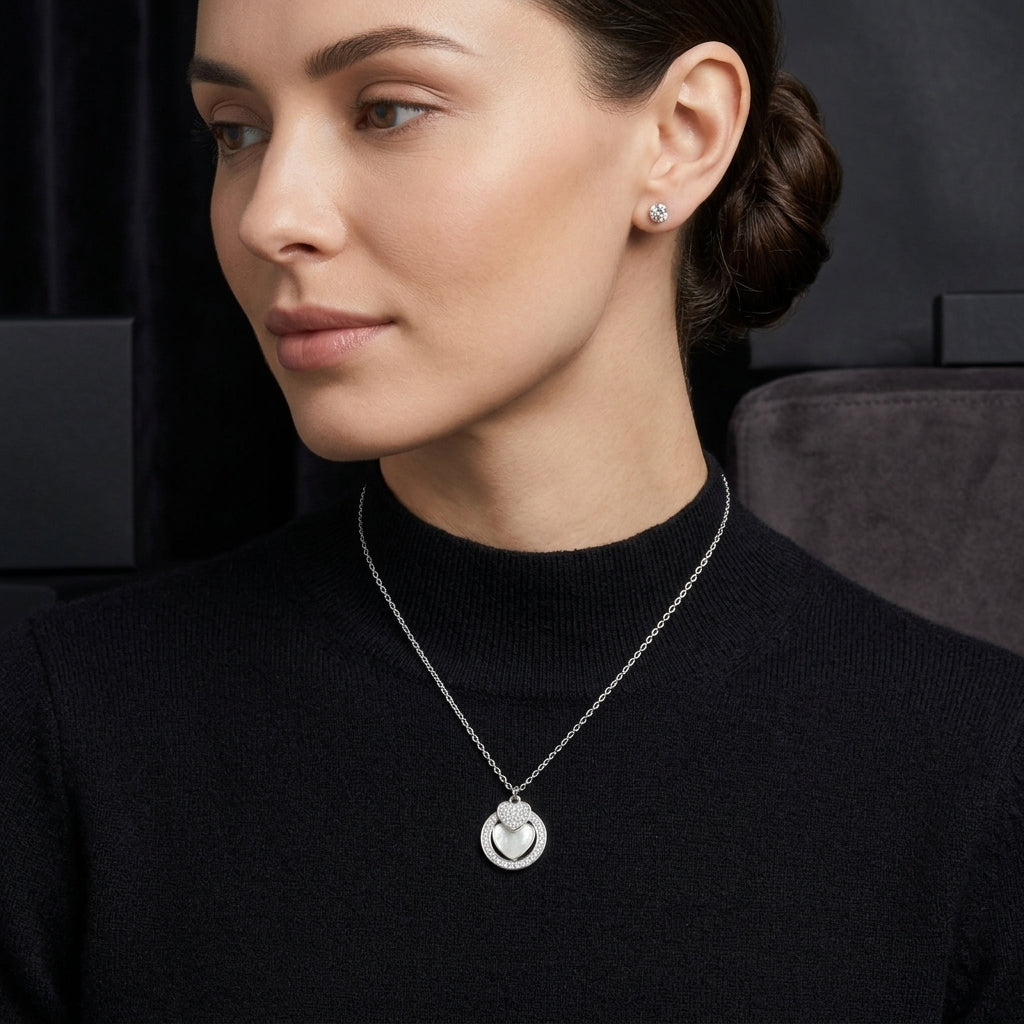 A woman wearing a delicate silver pendant necklace with a circular cutout design and a matching stud earring, dressed in a black mock-neck top against a dark background.
