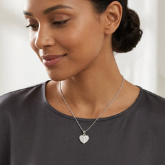 A woman wearing a delicate silver heart pendant necklace on a fine chain, paired with a dark gray crewneck top.