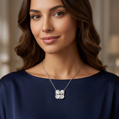 A woman wearing a silver four-leaf clover pendant necklace, shown from the chest up against a softly blurred indoor background.