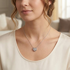 A close-up of a woman wearing a delicate silver heart pendant necklace with a clear stone, styled with a cream-colored scoop-neck top.