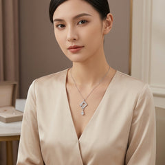 A woman wearing a delicate silver-toned necklace with a geometric pendant and clear stones, paired with a beige satin V-neck top in an elegant indoor setting.