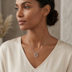 A woman wearing a delicate silver teardrop pendant necklace with a small central gemstone, styled with a cream-colored V-neck top.