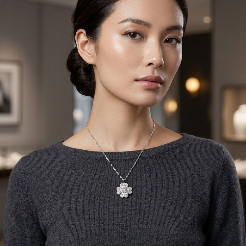 A woman wearing a delicate silver-tone floral pendant necklace with clear stones, styled with a dark gray knit top in a softly blurred boutique setting.