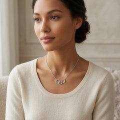 A woman wearing a delicate silver necklace with three interlocking rings, styled with a cream-colored knit top in a softly lit indoor setting.